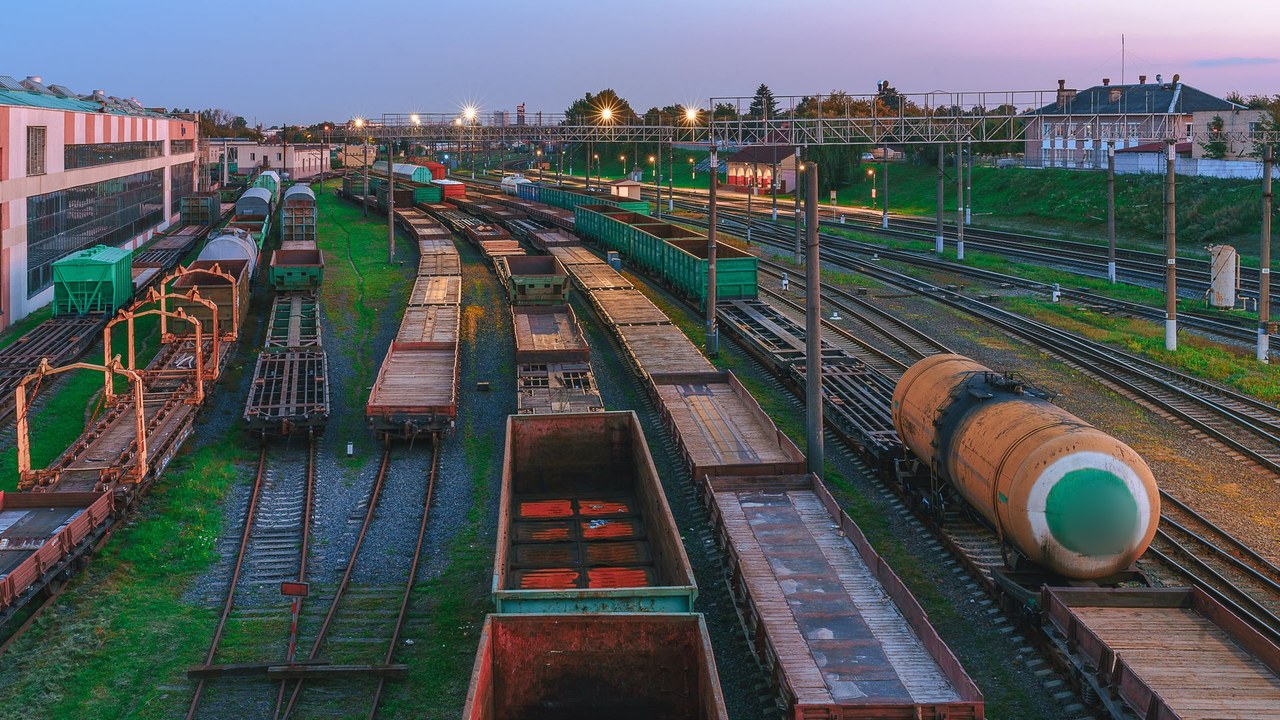 Rail freight yard at dusk with rows of cargo wagons and a tank wagon under floodlights