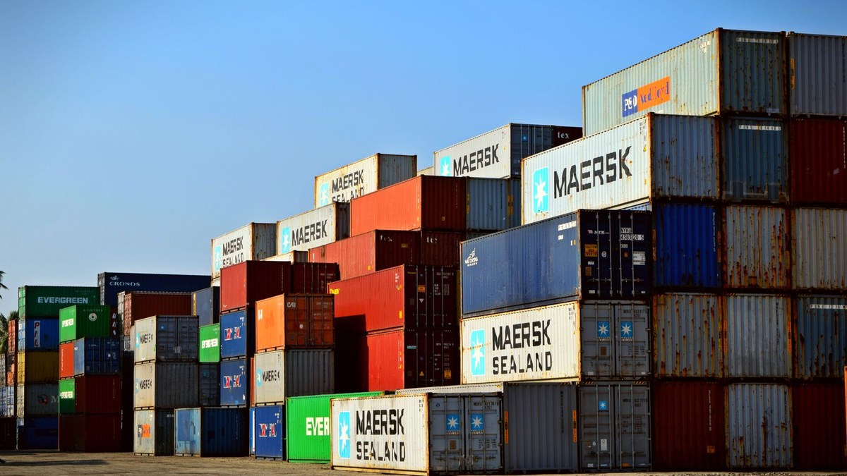 Stacked multicoloured shipping containers in a sunny port yard under a clear blue sky