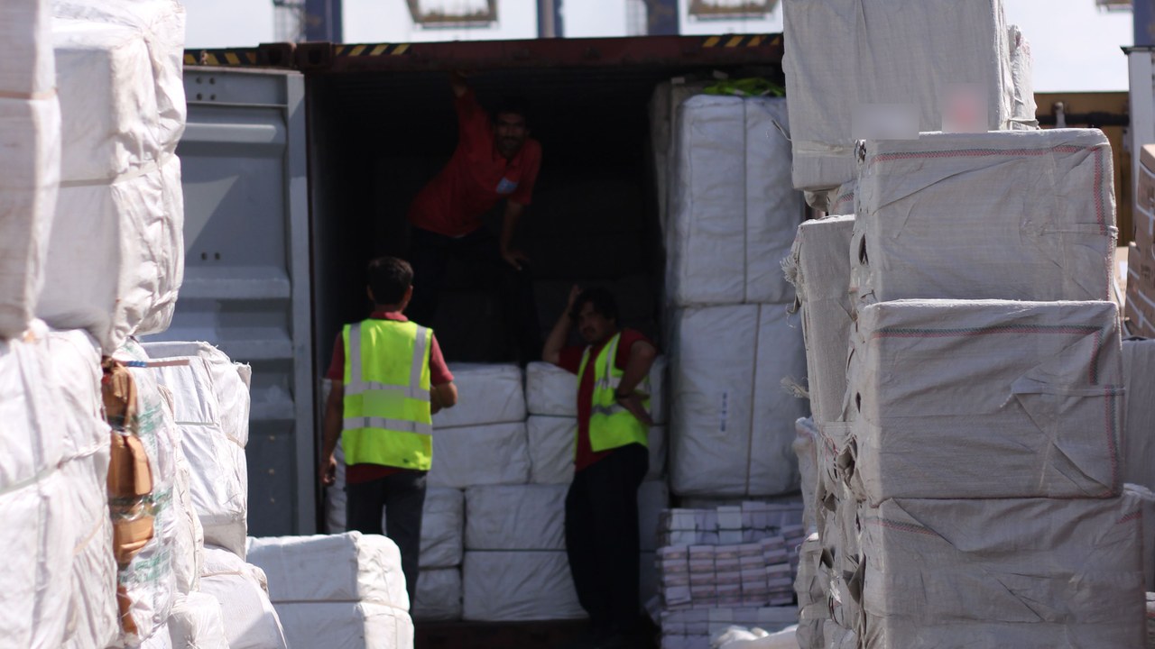 Port workers loading wrapped export bales into an open shipping container
