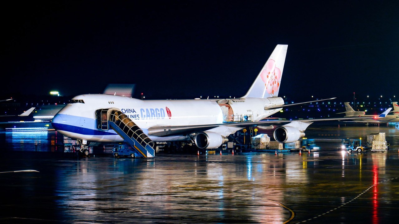 Cargo freighter being loaded with pallets on a wet airport apron at night