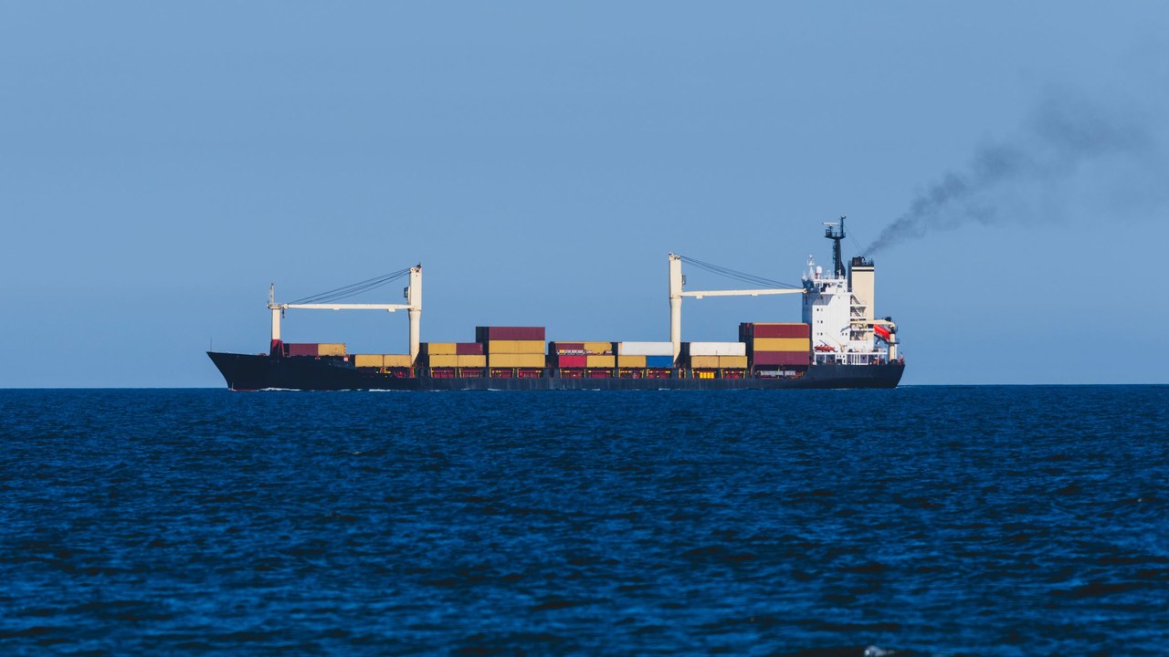 Container ship at sea with exhaust smoke rising from its funnel against a clear blue sky