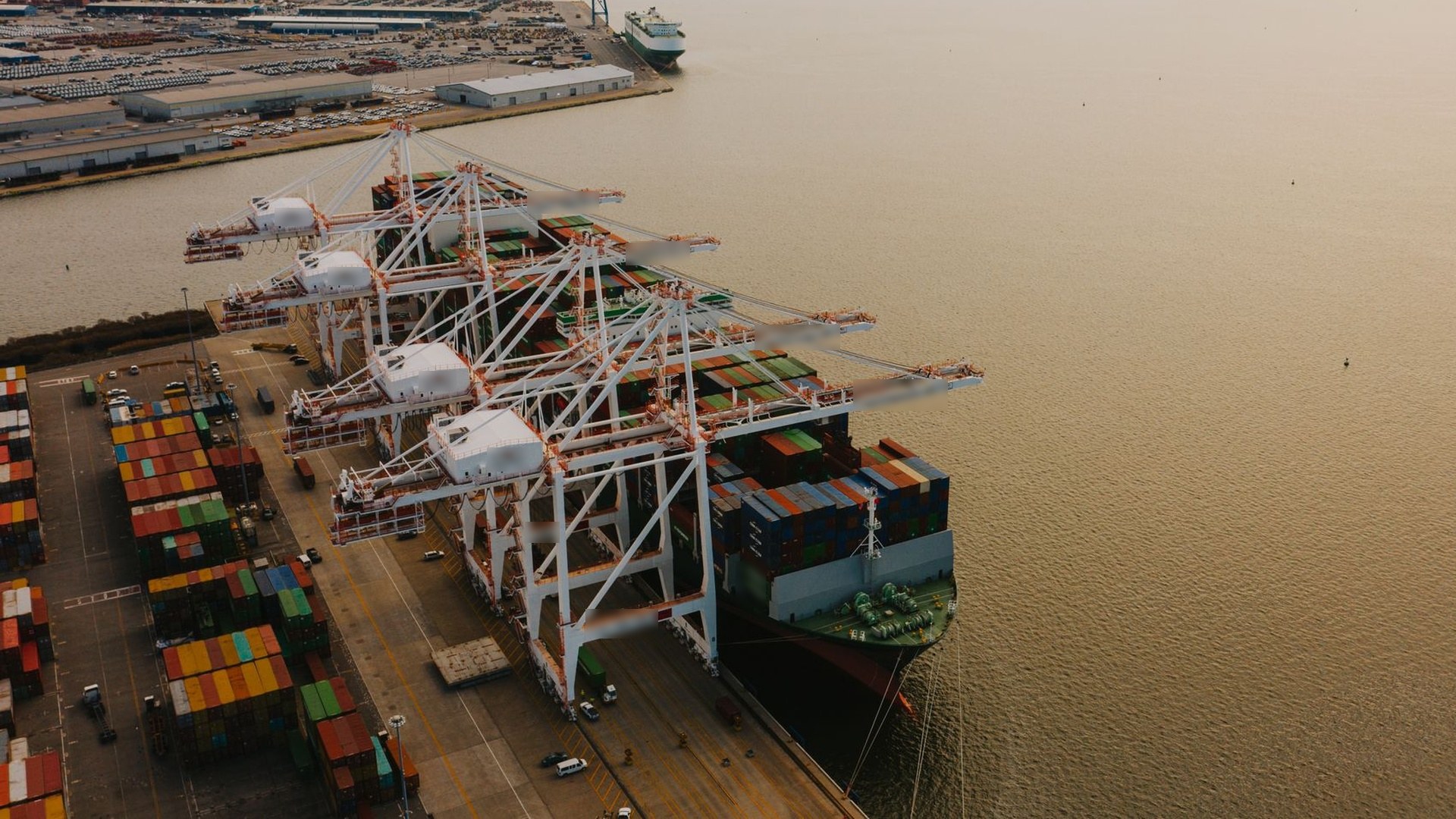 Aerial view of a large container ship being loaded by a row of gantry cranes at a busy transshipment terminal