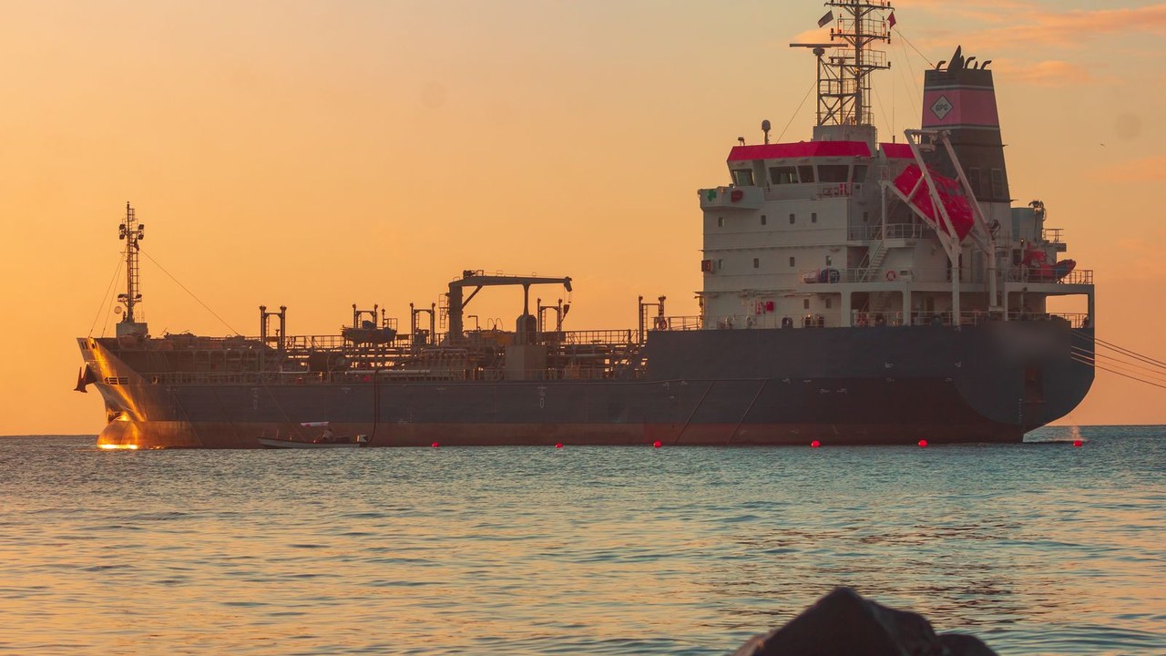Product tanker at anchor close to shore at sunset with calm water in the foreground