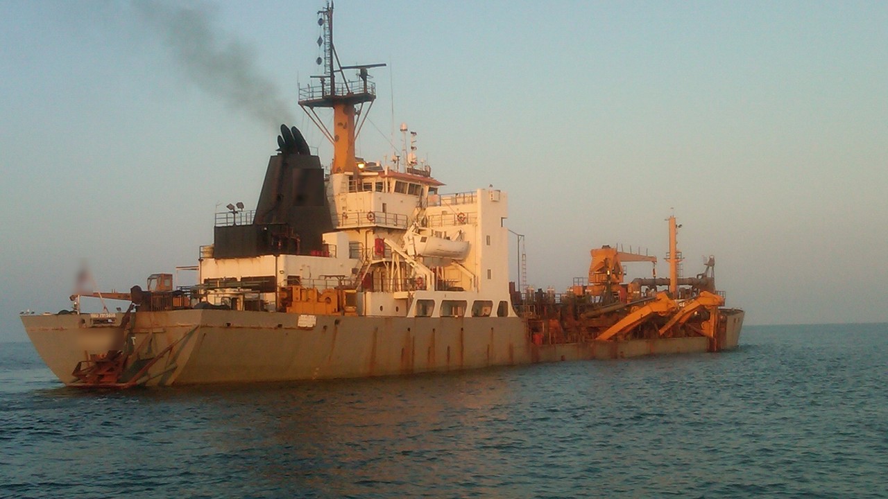 Trailing suction hopper dredger working at sea in soft evening light, with orange dredging arms along its side