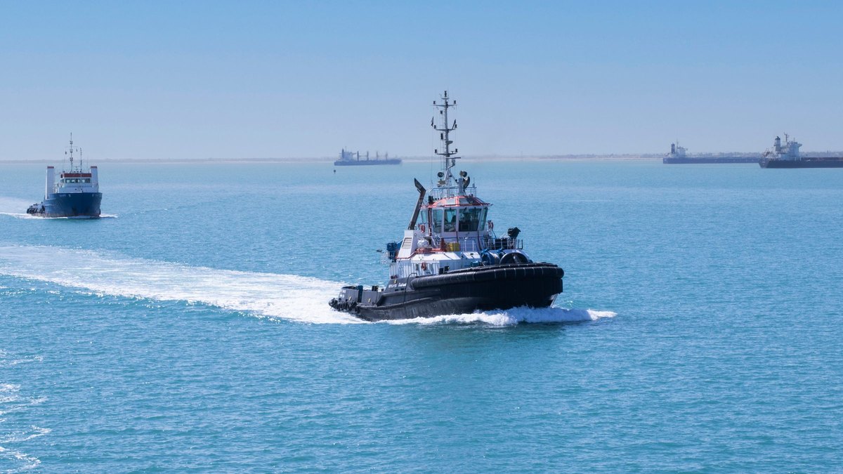 Tugboat speeding across blue water in the Suez Canal with cargo ships waiting on the horizon